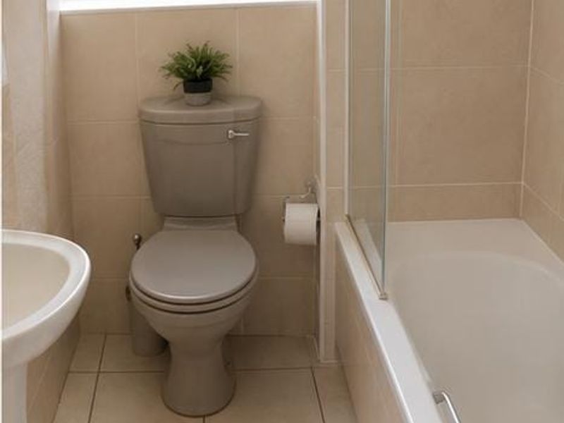A functional bathroom featuring a pedestal sink, toilet, and a bathtub with a glass shower screen, finished with neutral wall and floor tiles.