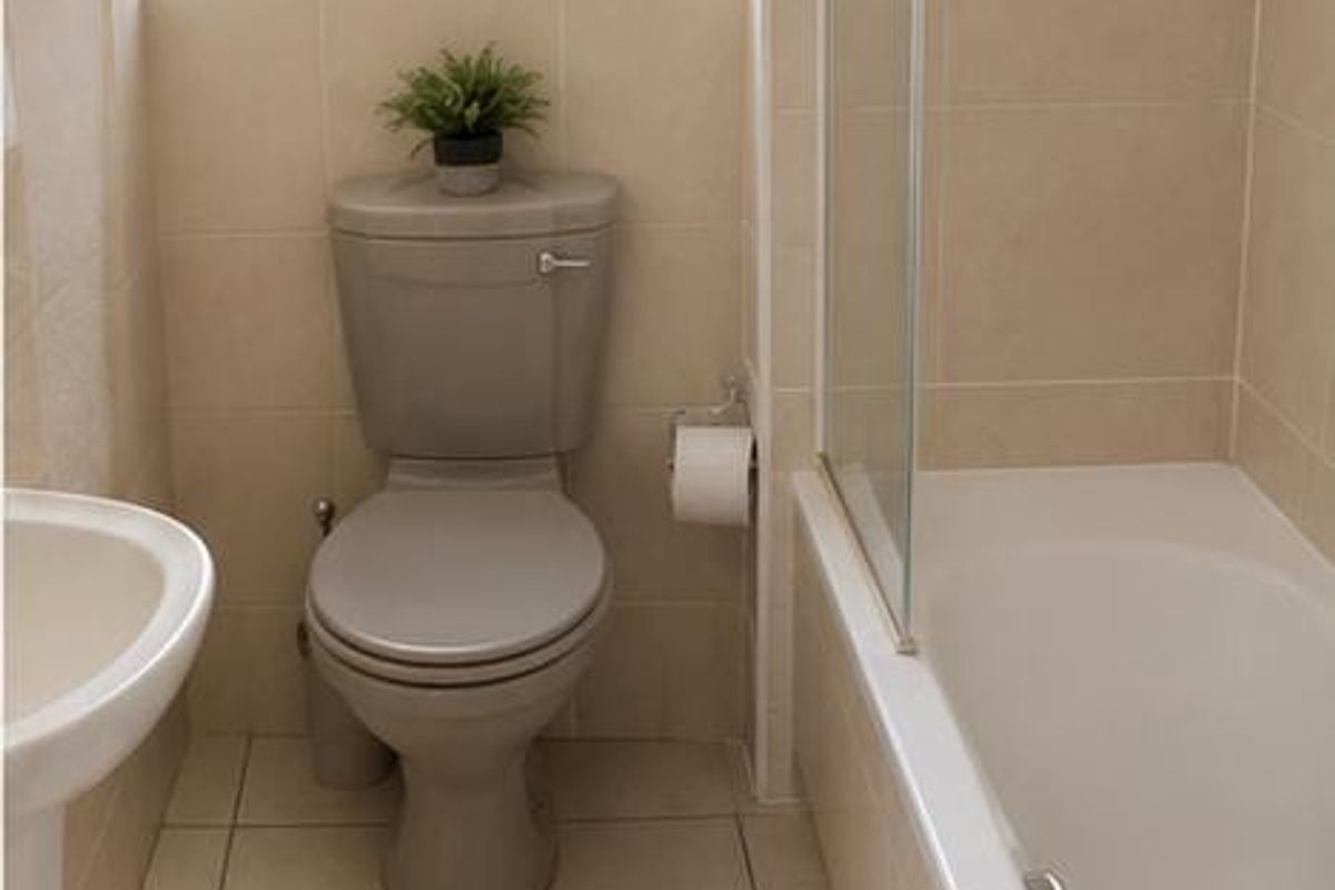 A functional bathroom featuring a pedestal sink, toilet, and a bathtub with a glass shower screen, finished with neutral wall and floor tiles.