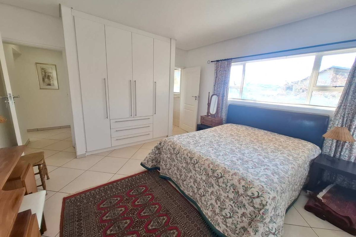 A spacious bedroom featuring built-in white cabinetry, tiled flooring, and a large window providing natural light.