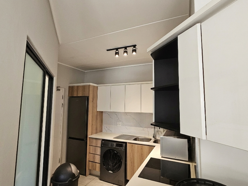 Modern kitchen featuring sleek two-tone cabinetry, wood-grain accents, integrated appliances, and contemporary track lighting in a compact, functional layout.