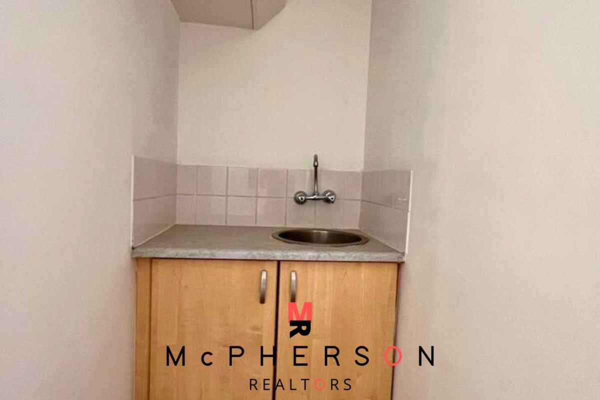 A compact kitchenette area featuring built-in cabinetry, a stainless steel sink, and a tiled backsplash.