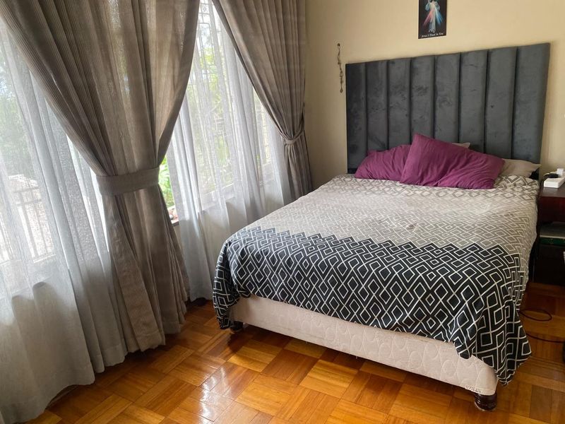 A well-maintained bedroom featuring classic parquet flooring and large windows with security bars, providing natural light and a comfortable living space.