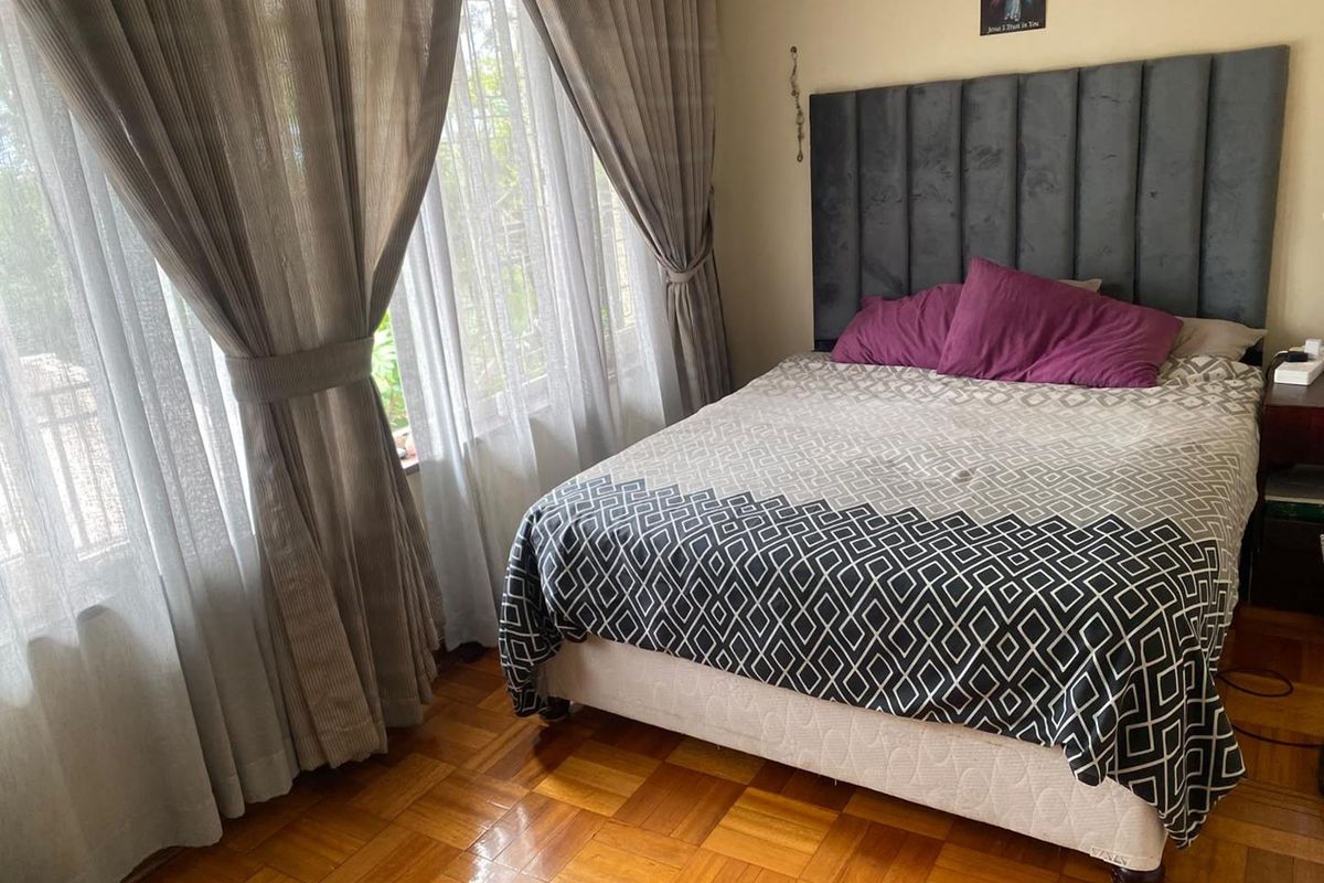 A well-maintained bedroom featuring classic parquet flooring and large windows with security bars, providing natural light and a comfortable living space.