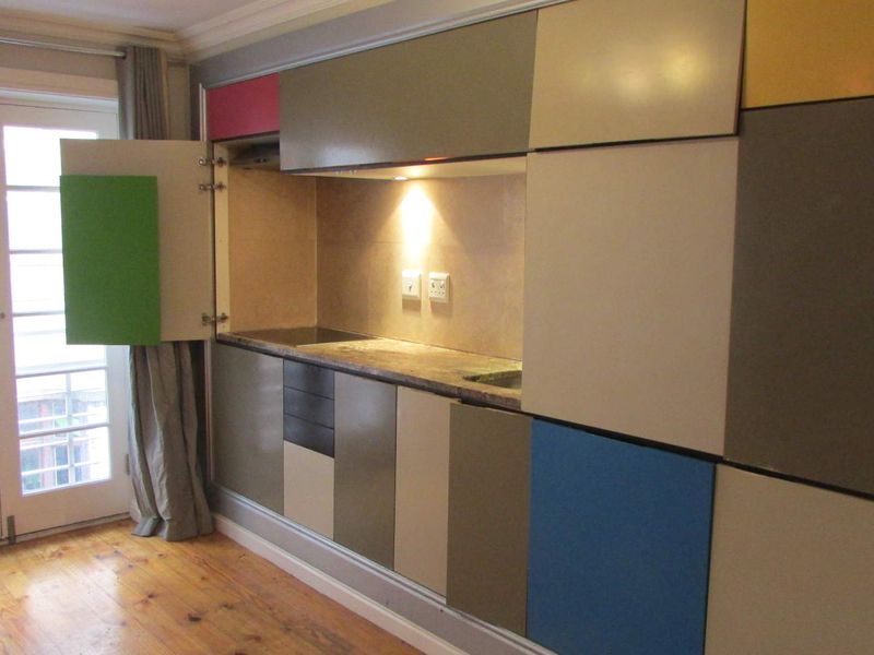Compact kitchen unit featuring multi-colored cabinetry, integrated workspace, and direct access to a balcony through glass paneled doors.