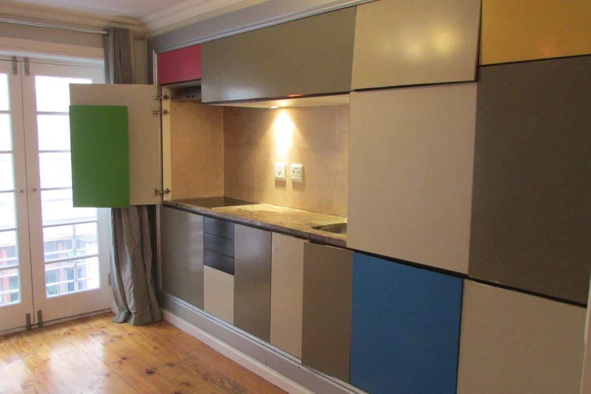 Compact kitchen unit featuring multi-colored cabinetry, integrated workspace, and direct access to a balcony through glass paneled doors.
