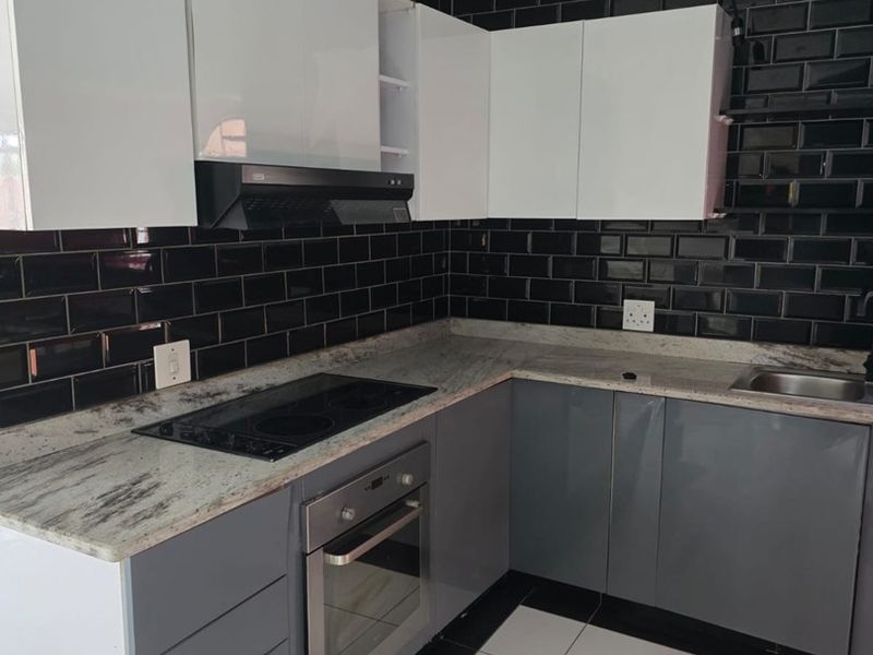 Modern kitchen featuring high-gloss cabinetry, granite countertops, a built-in oven, electric hob, and striking black subway tile backsplash.