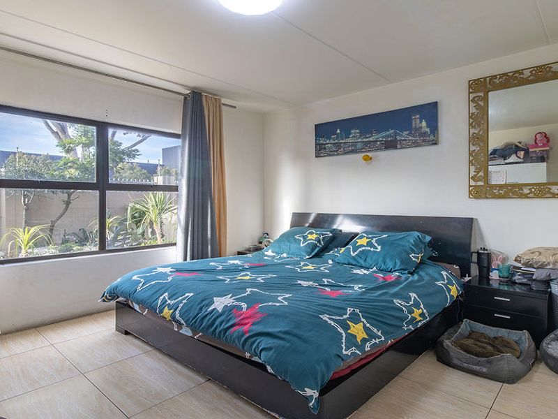 A well-lit bedroom featuring large windows with curtain tracks and neutral tiled flooring, offering a comfortable and functional living space.