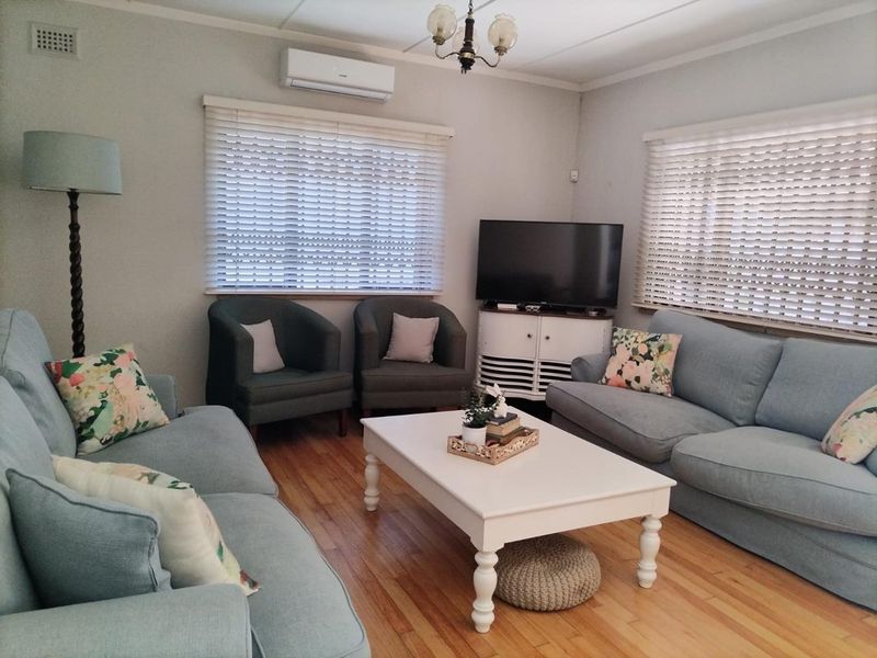 A comfortable living room featuring polished hardwood flooring, dual windows with venetian blinds, and a wall-mounted split-system air conditioning unit.