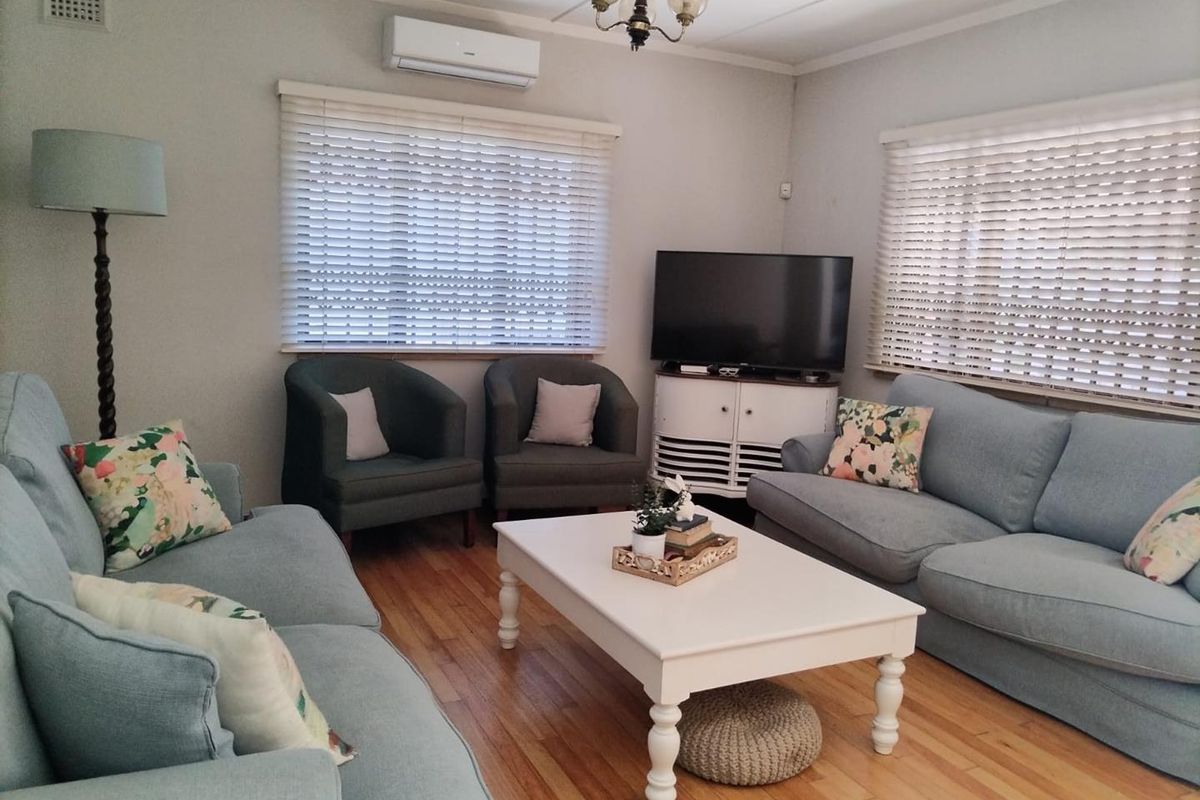 A comfortable living room featuring polished hardwood flooring, dual windows with venetian blinds, and a wall-mounted split-system air conditioning unit.