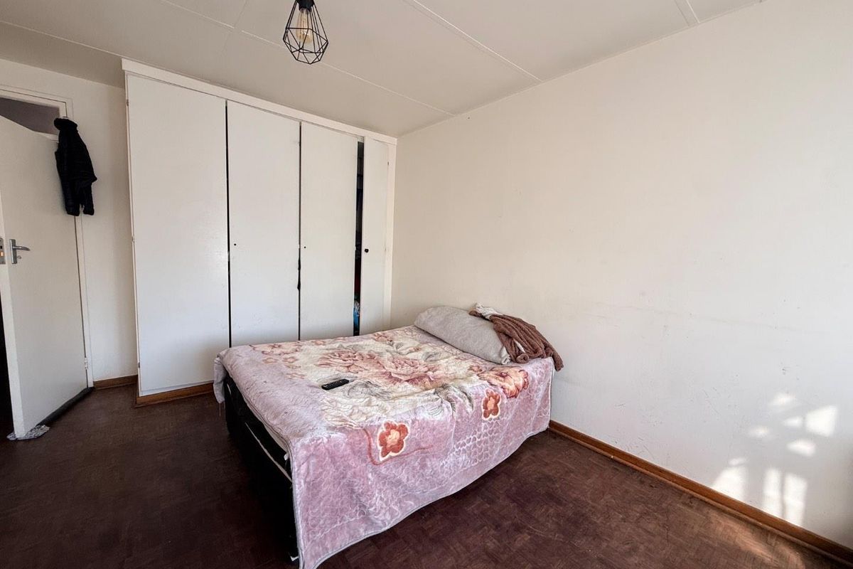 A bedroom featuring parquet flooring, a built-in wardrobe, and a pendant light fixture, offering a functional space ready for cosmetic updates.