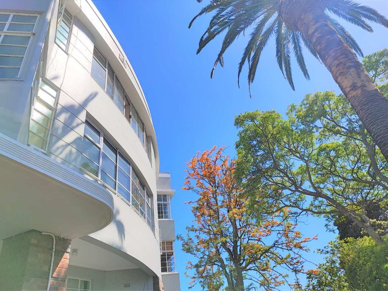 A low-angle view of the apartment building's curved white facade, featuring multi-pane windows and mature trees in the foreground.