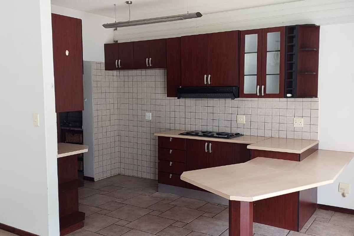 A functional kitchen featuring dark wood cabinetry, a built-in gas hob, extractor fan, and a breakfast bar peninsula with tiled flooring.