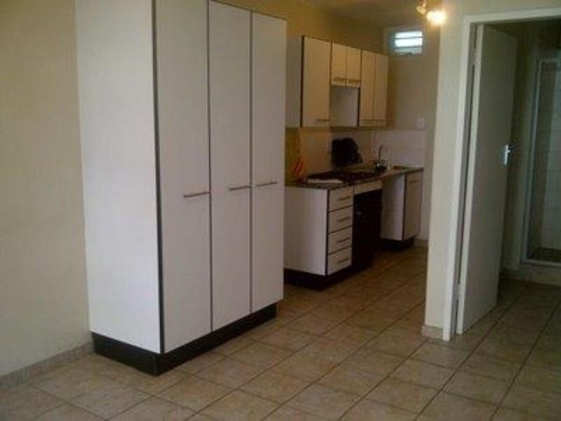 A compact kitchen area featuring built-in cabinetry, a stove, and tiled flooring, adjacent to a built-in wardrobe in an open-plan layout.
