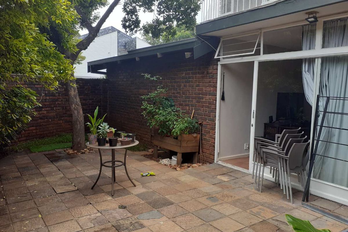 A private rear courtyard featuring a paved patio area, brick boundary walls, and direct access to the interior via a sliding glass door.