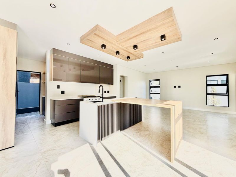 Modern open-plan kitchen featuring a central island with breakfast bar, sleek cabinetry, stone countertops, and a distinctive timber ceiling feature with recessed lighting.