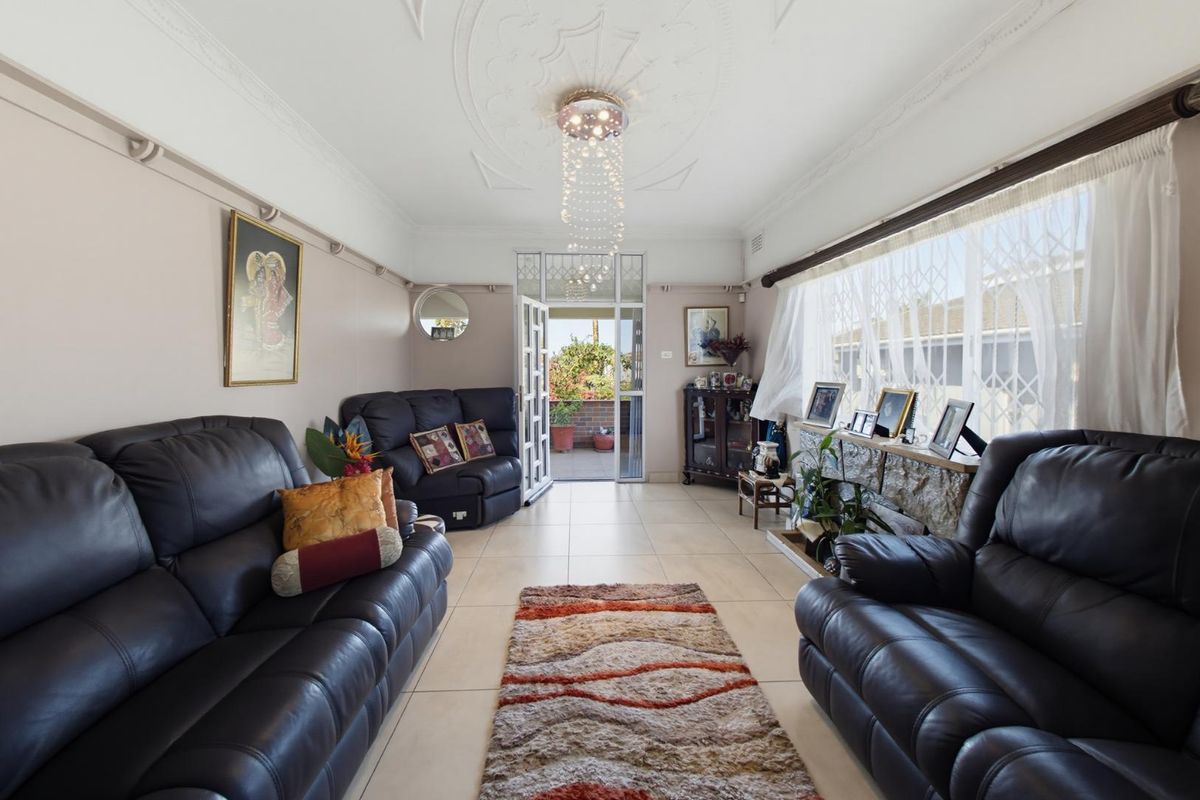 A living room featuring ornate ceiling detailing, tiled flooring, and direct access to an outdoor patio area through a sliding glass door.