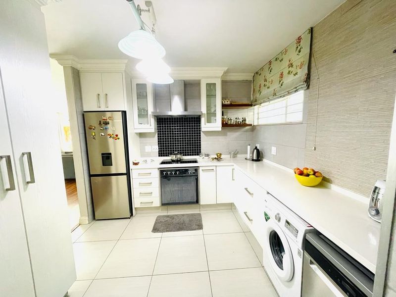 A well-maintained kitchen featuring white cabinetry, stone countertops, a tiled backsplash, and integrated appliances including an oven, hob, washing machine, and dishwasher.