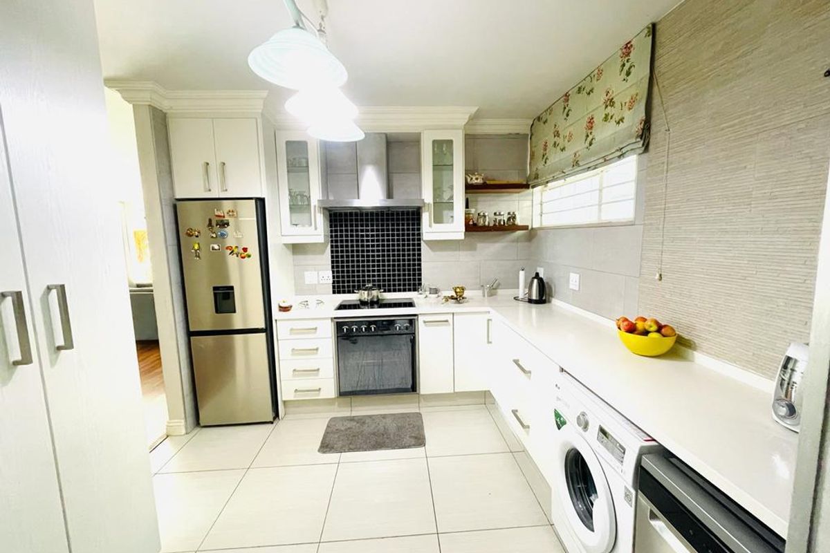 A well-maintained kitchen featuring white cabinetry, stone countertops, a tiled backsplash, and integrated appliances including an oven, hob, washing machine, and dishwasher.