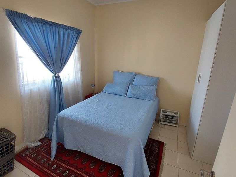 A functional bedroom featuring tiled flooring, a built-in wardrobe, and a window with curtains, providing a simple and practical living space.