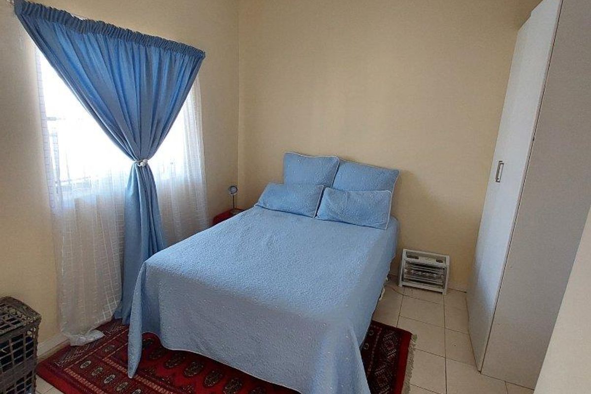 A functional bedroom featuring tiled flooring, a built-in wardrobe, and a window with curtains, providing a simple and practical living space.