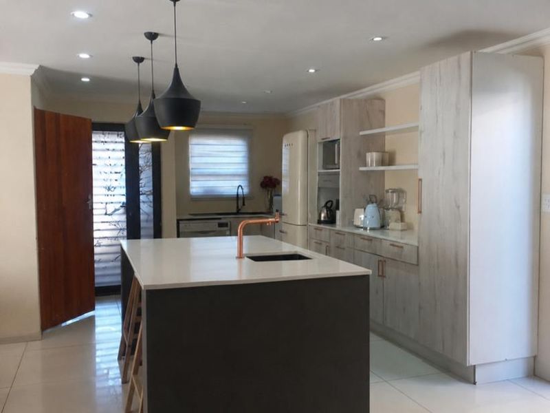 Modern kitchen featuring a central island with a copper faucet, sleek cabinetry, recessed lighting, and tiled flooring.