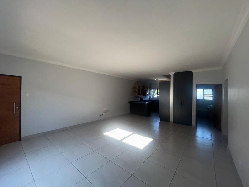 Spacious open-plan living area featuring neutral tiled flooring, built-in kitchen cabinetry, and integrated storage cupboards, offering a clean and versatile layout.