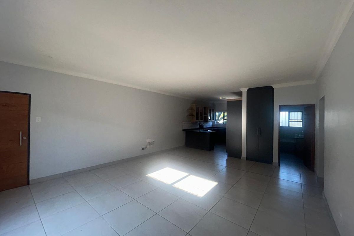 Spacious open-plan living area featuring neutral tiled flooring, built-in kitchen cabinetry, and integrated storage cupboards, offering a clean and versatile layout.