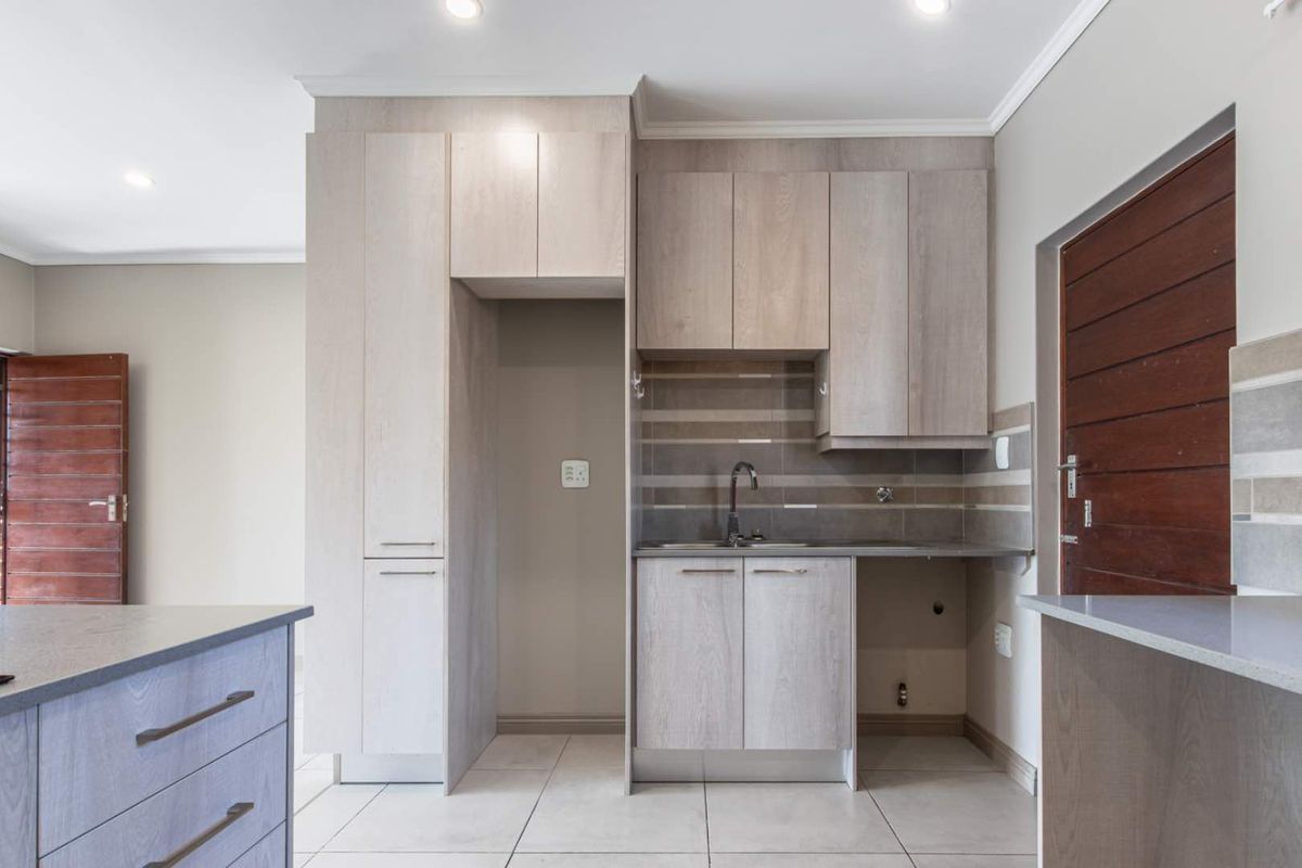 Modern kitchen area featuring light wood-tone cabinetry, tiled splashback, and integrated sink, offering a clean and functional space ready for appliances.