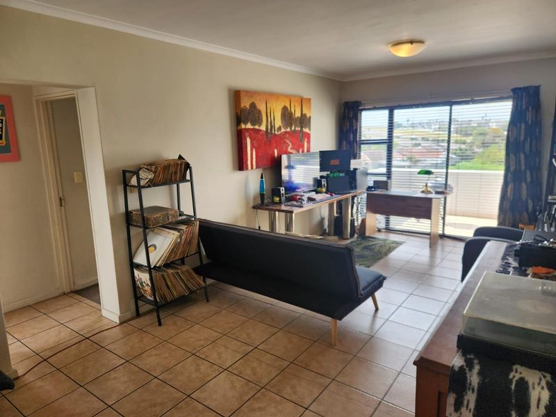 A living room area featuring tiled flooring and a large sliding glass door providing access to a balcony and natural light.