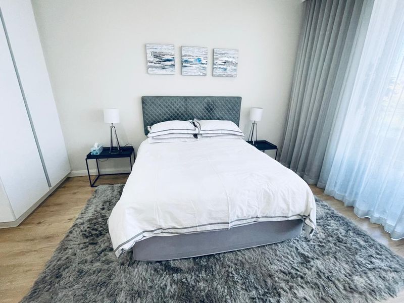 A well-maintained bedroom featuring light-toned laminate flooring, a built-in wardrobe, and floor-to-ceiling curtains providing ample natural light.