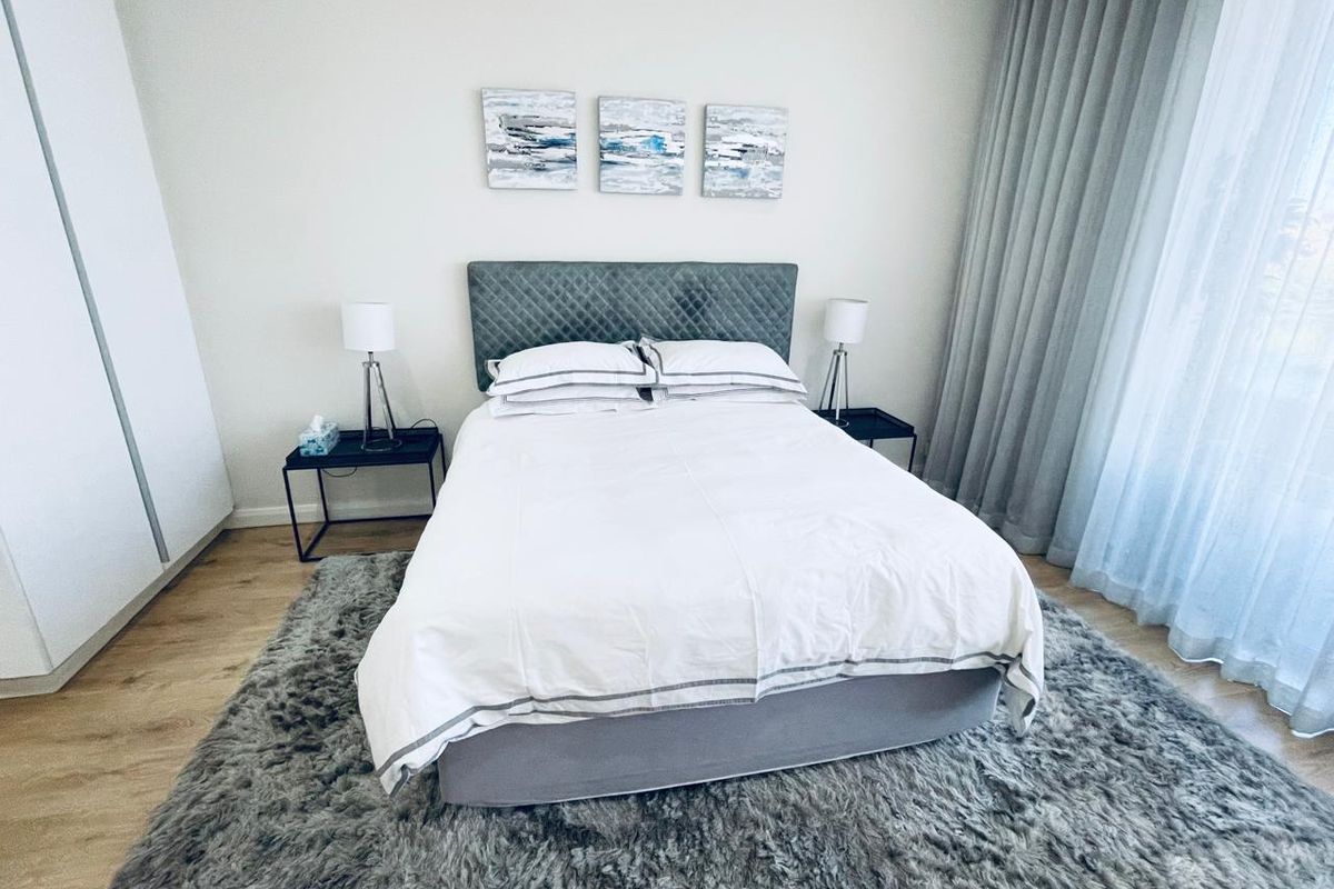 A well-maintained bedroom featuring light-toned laminate flooring, a built-in wardrobe, and floor-to-ceiling curtains providing ample natural light.