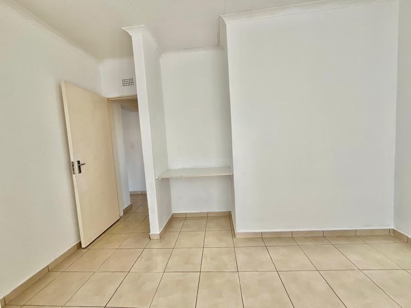 An empty bedroom featuring tiled flooring, a built-in desk nook, and neutral white walls, offering a blank canvas for personalization.