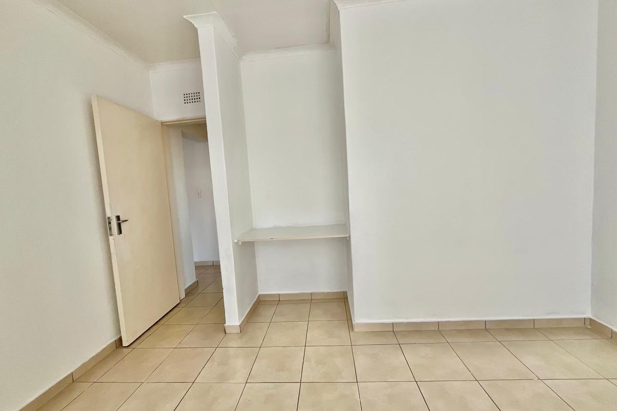 An empty bedroom featuring tiled flooring, a built-in desk nook, and neutral white walls, offering a blank canvas for personalization.
