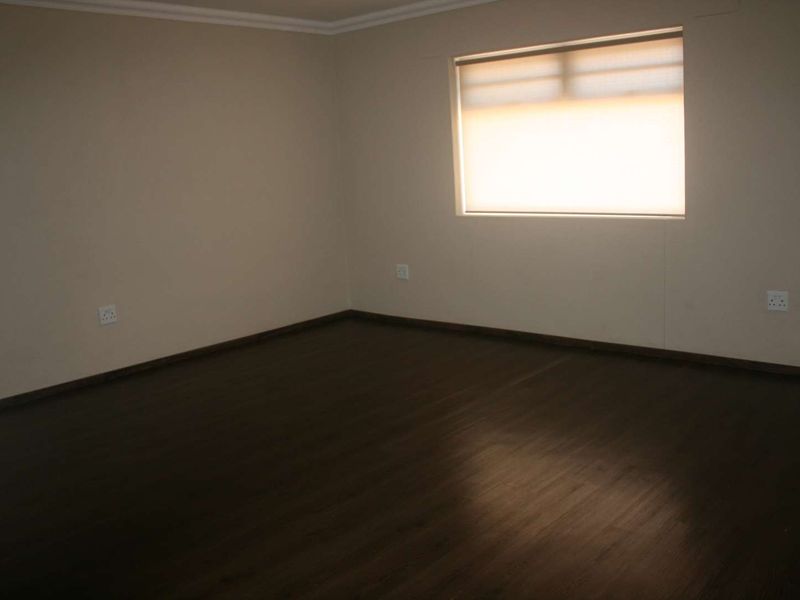 A spacious, empty bedroom featuring dark laminate flooring, neutral walls, and a fitted roller blind, providing a clean canvas for personalization.