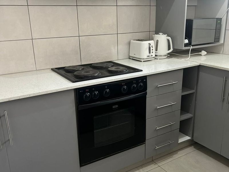 Modern kitchen featuring grey cabinetry, stone countertops, tiled backsplash, and integrated appliances including an electric stove, oven, and extractor fan.