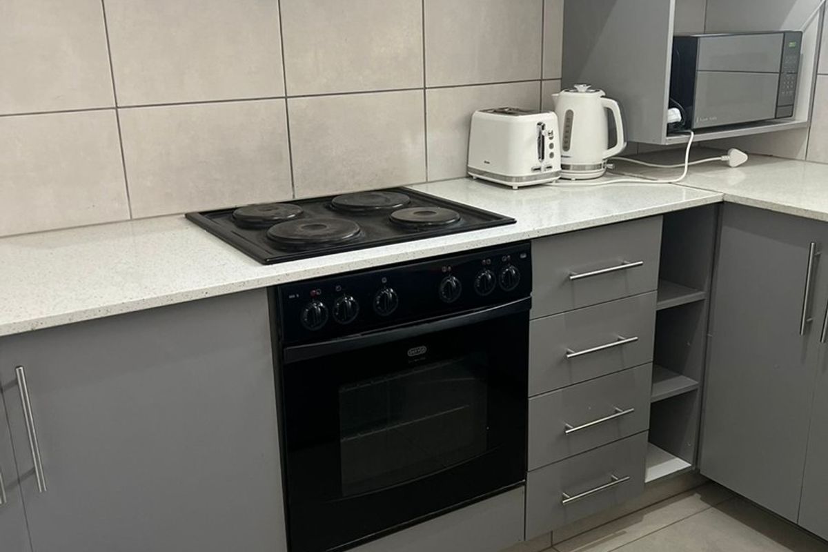 Modern kitchen featuring grey cabinetry, stone countertops, tiled backsplash, and integrated appliances including an electric stove, oven, and extractor fan.