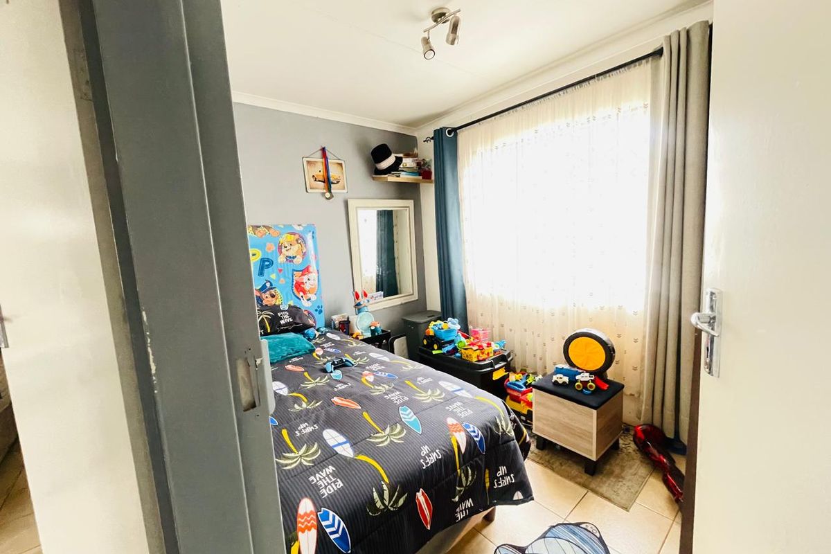 A functional bedroom featuring tiled flooring, a large window with curtain tracks, and a ceiling-mounted light fixture.