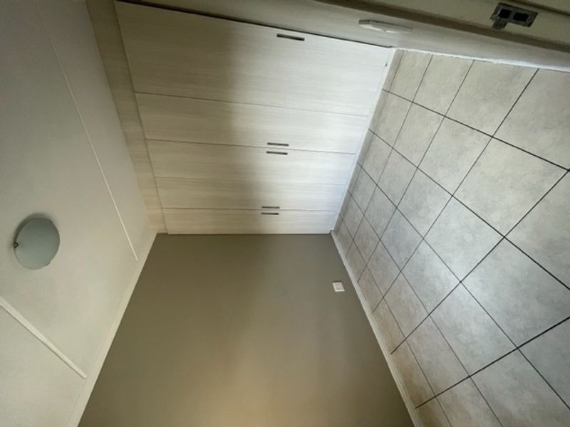 A clean, empty bedroom featuring neutral tiled flooring and modern built-in cupboards with light wood-grain finish.