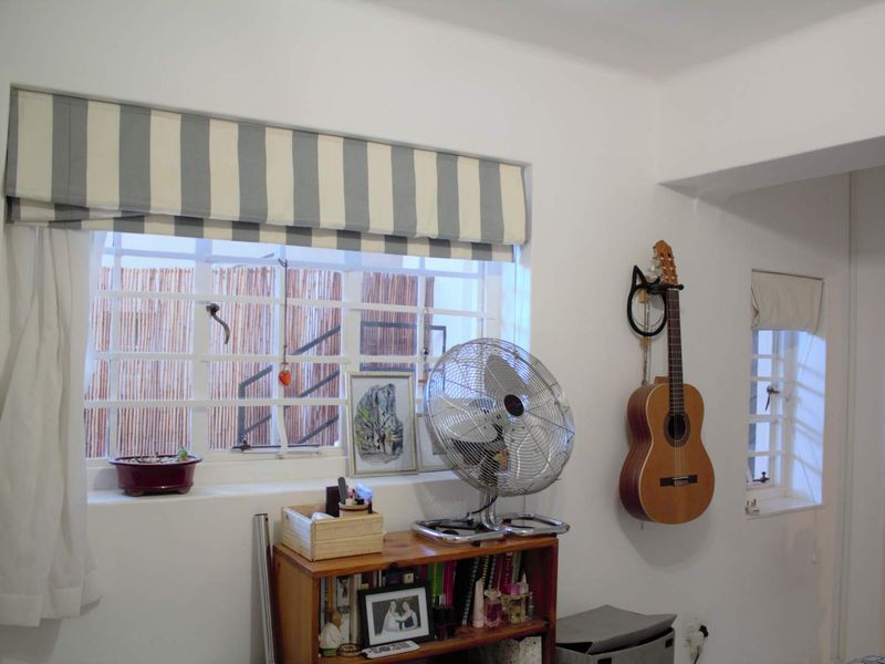 A living area featuring white walls, security bars on the windows, and striped roman blinds, providing a functional and bright space.