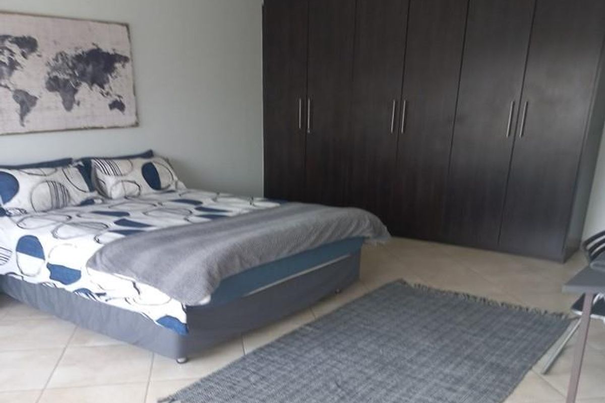 A spacious bedroom featuring large dark wood built-in cupboards and neutral tiled flooring.