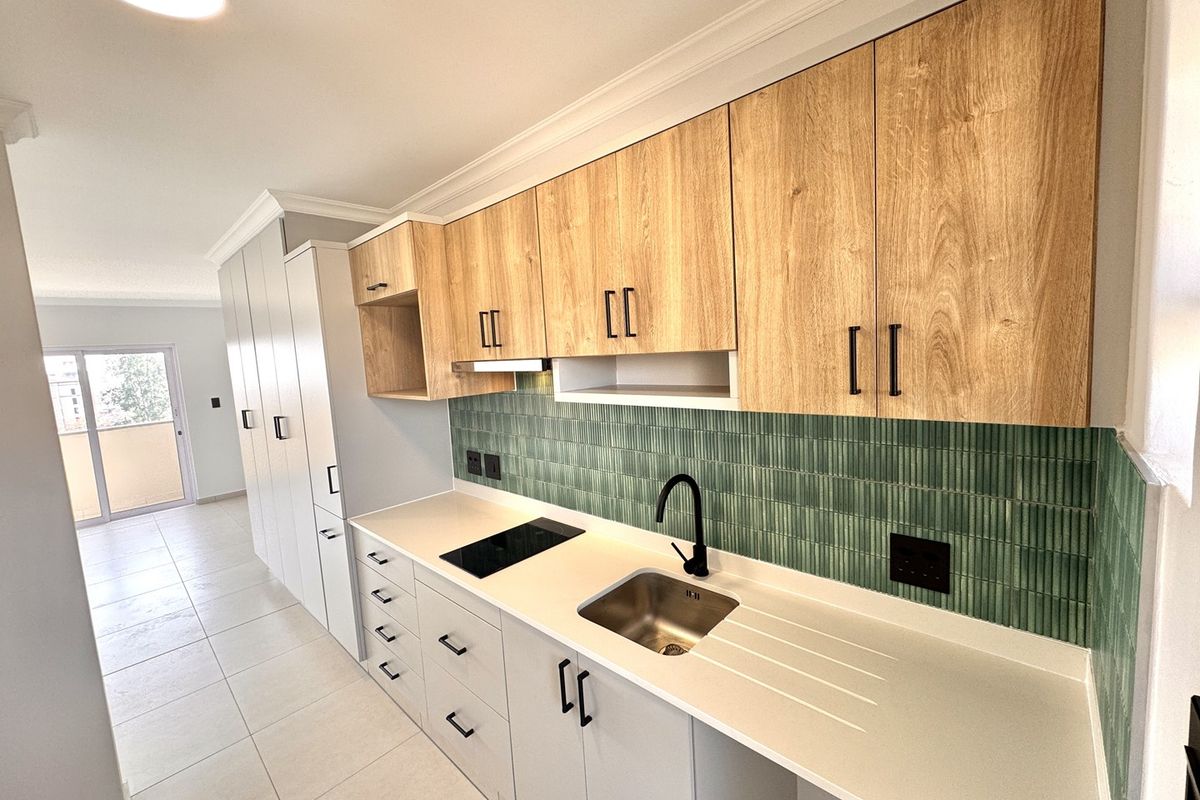 Modern kitchen featuring light wood-grain upper cabinets, sleek white lower cabinetry, stone countertops, a green tiled backsplash, and integrated appliances.