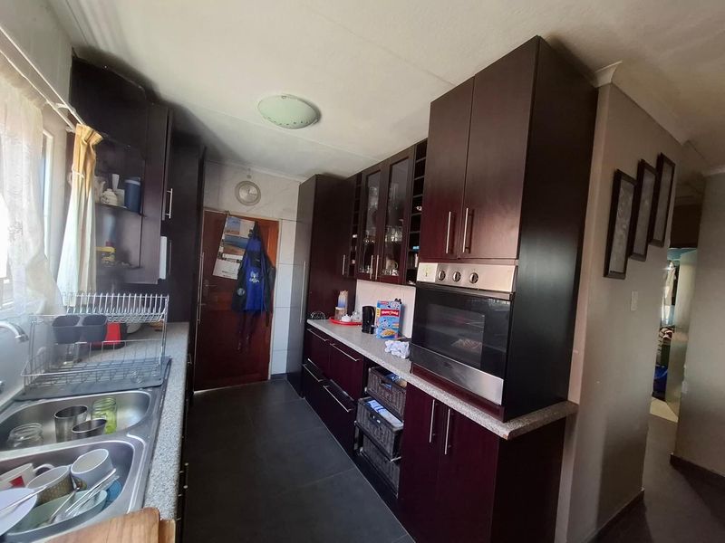 A functional kitchen featuring dark wood cabinetry, built-in oven, double stainless steel sink, and stone-look countertops with tiled flooring.