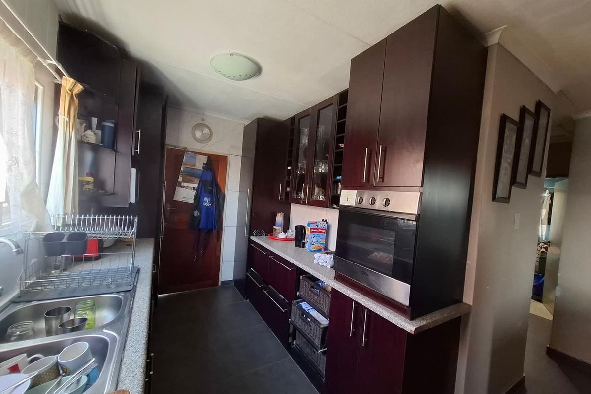A functional kitchen featuring dark wood cabinetry, built-in oven, double stainless steel sink, and stone-look countertops with tiled flooring.