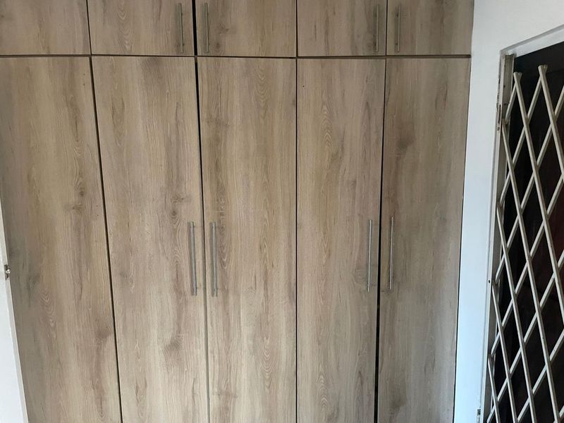 A bedroom featuring floor-to-ceiling built-in wooden cupboards with modern handles and an adjacent security gate.