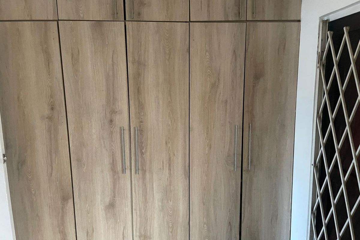 A bedroom featuring floor-to-ceiling built-in wooden cupboards with modern handles and an adjacent security gate.