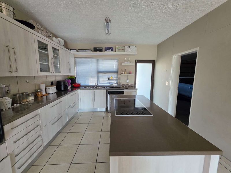 Modern kitchen featuring light wood-finish cabinetry, stone countertops, a central island with an integrated electric hob, and tiled flooring.