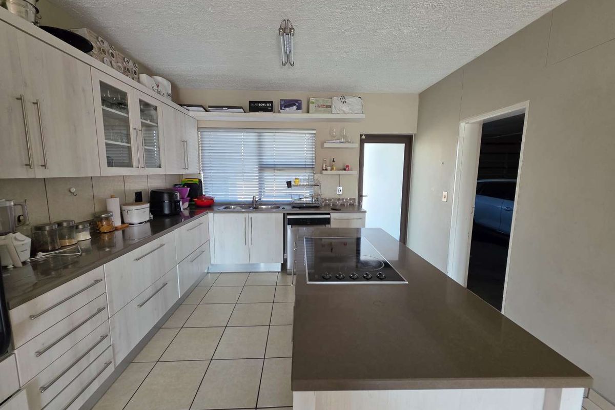 Modern kitchen featuring light wood-finish cabinetry, stone countertops, a central island with an integrated electric hob, and tiled flooring.