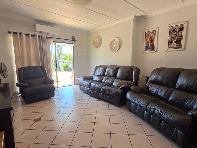 A spacious living room featuring tiled flooring, a split-system air conditioner, and a sliding glass door providing access to the outdoor area.