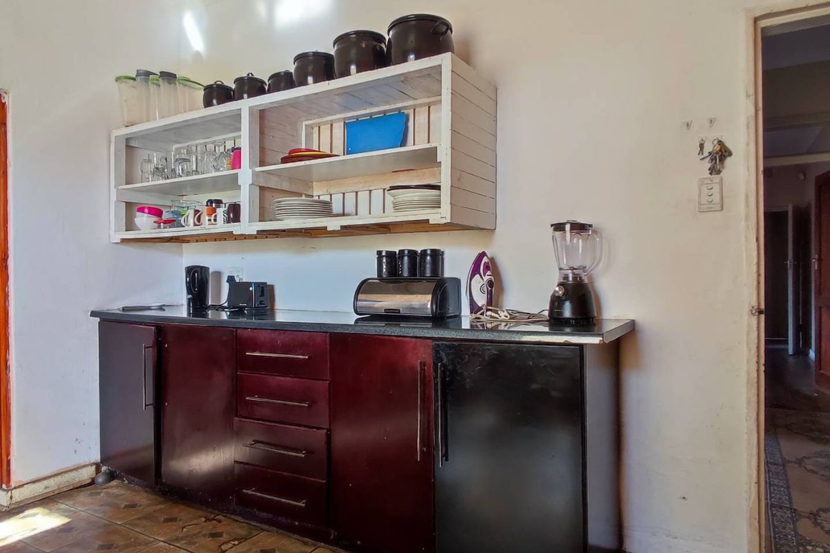 A functional kitchen area featuring dark built-in cabinetry, a laminate countertop, and open wall-mounted shelving units.
