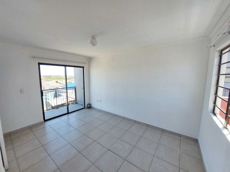 An empty bedroom featuring tiled flooring, a sliding glass door leading to a balcony, and a window with security bars.
